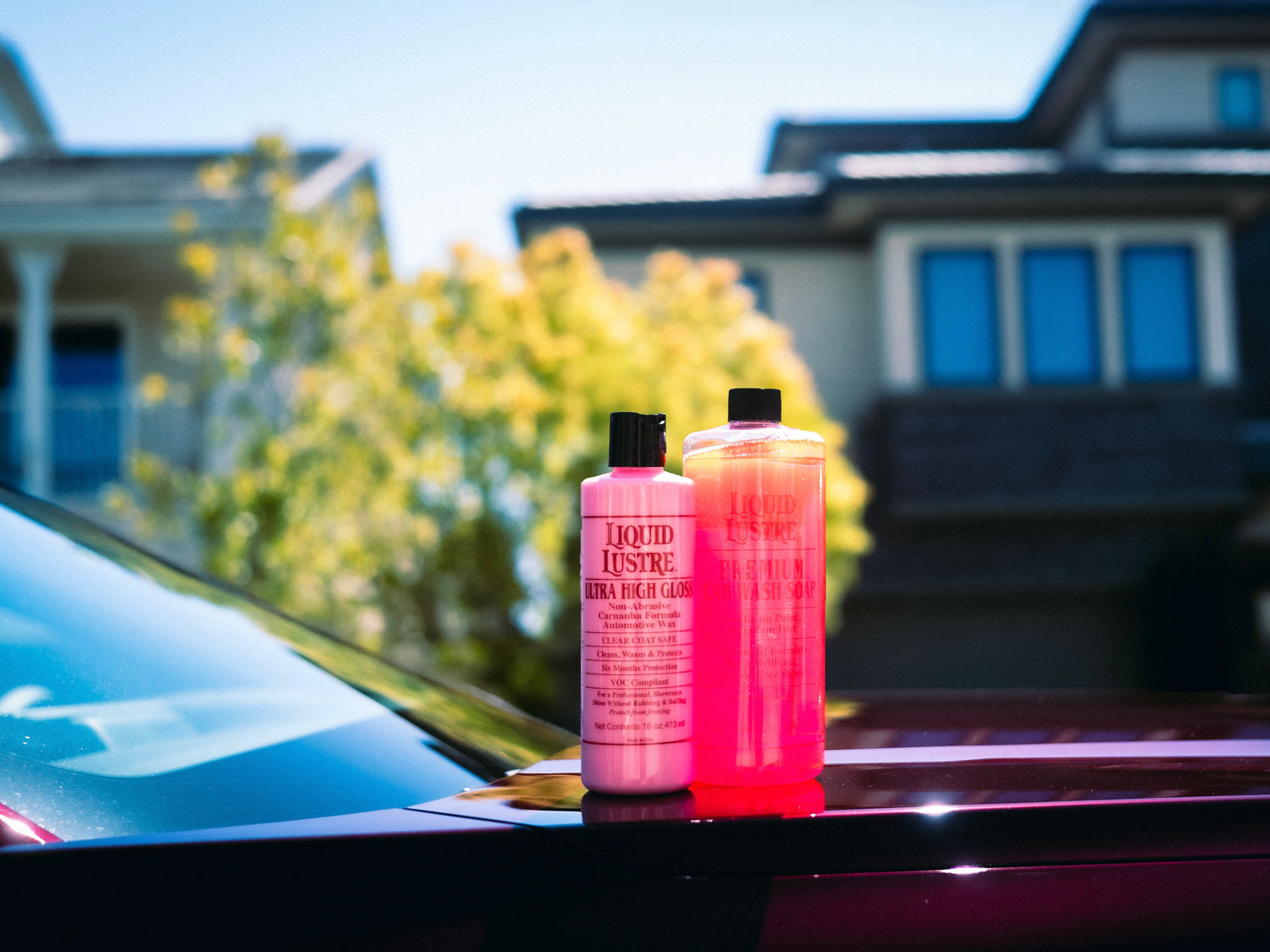 The liquid Lustre premium car care products against the backdrop of a car in outdoor setting