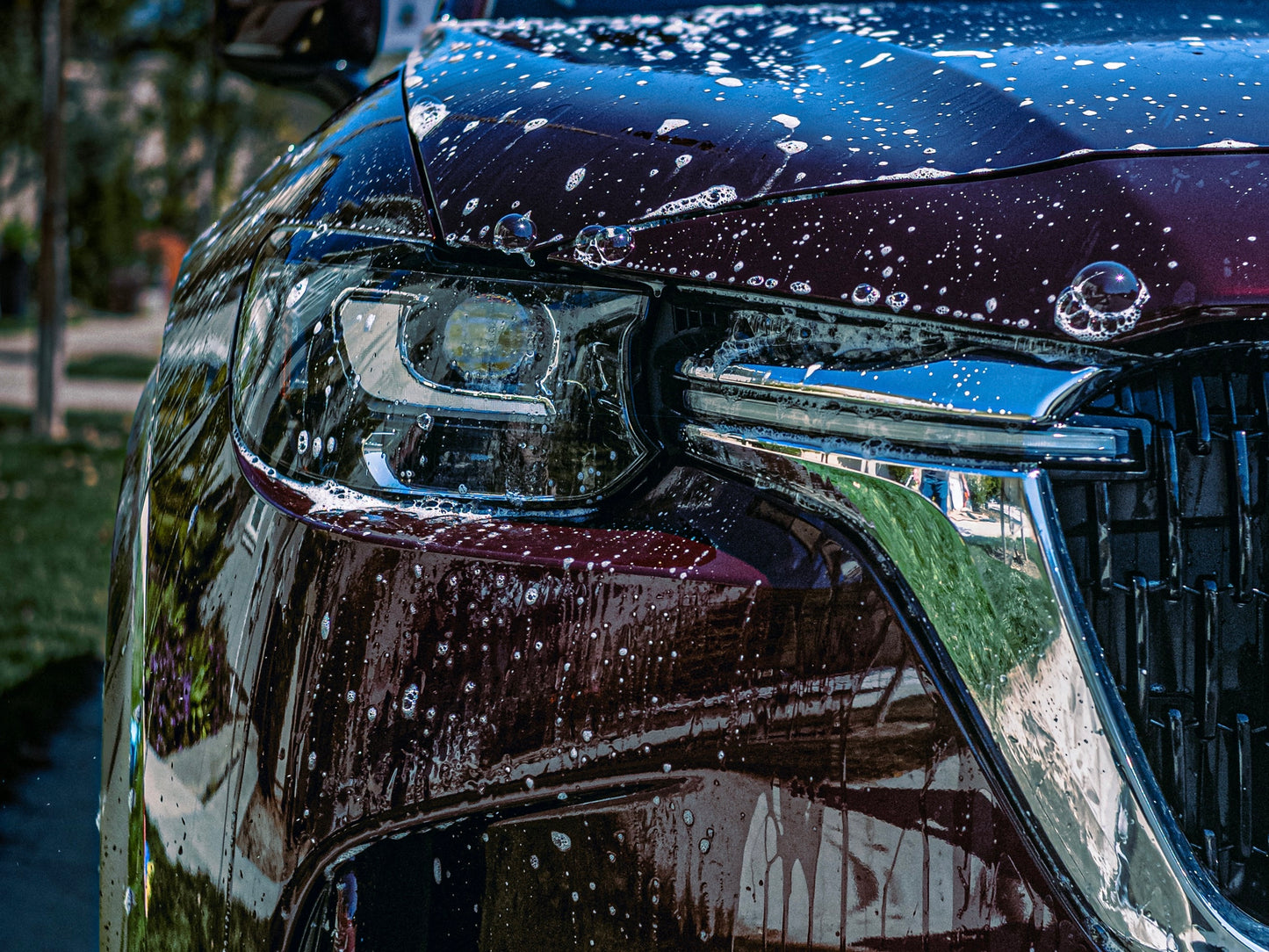 Close-up of a car's headlight and front grille with water droplets using the Liquid Lustre Ultra Clean car soap
