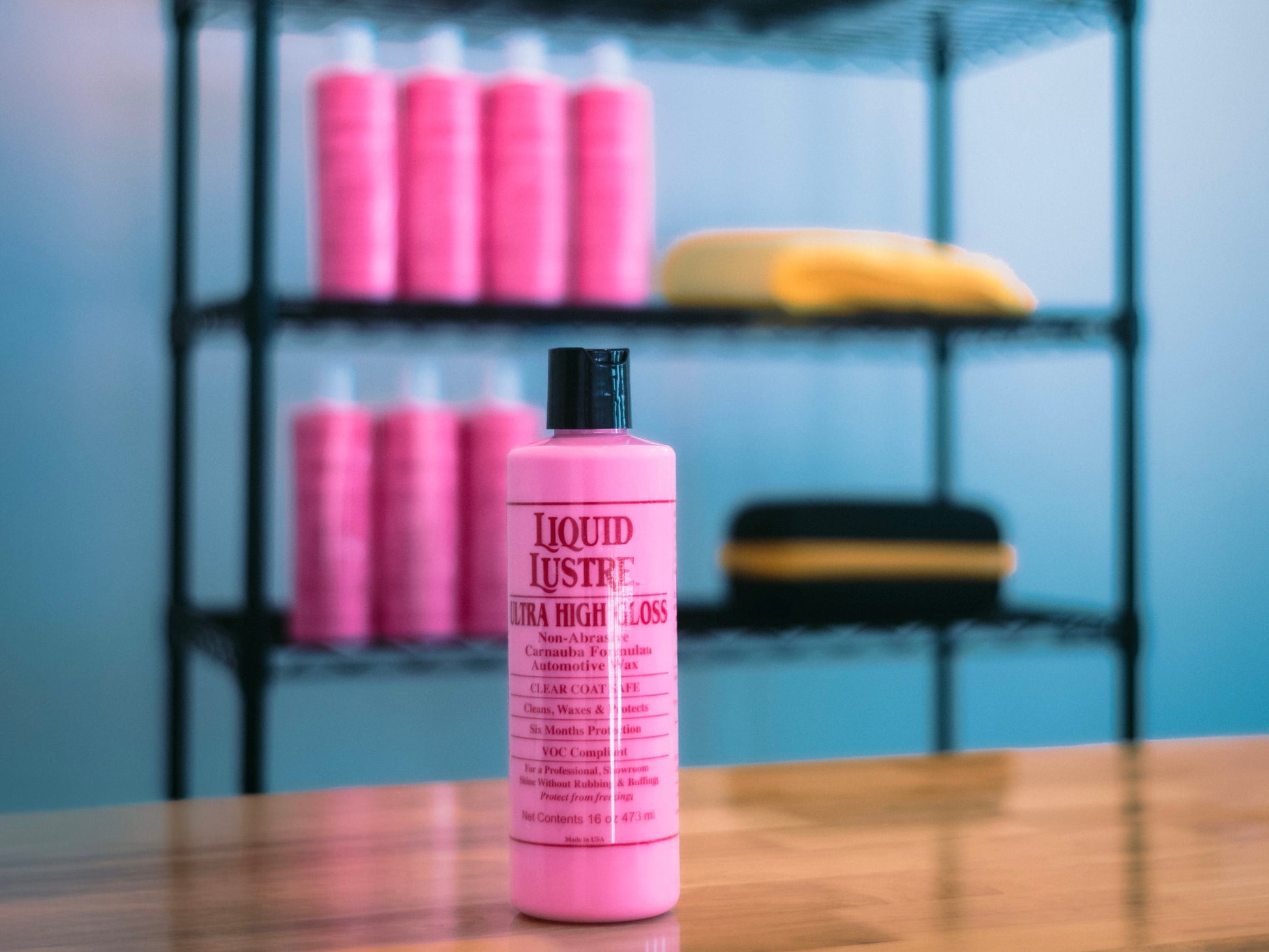 Pink bottle of Liquid Lustre on a wooden surface with shelves in the background.