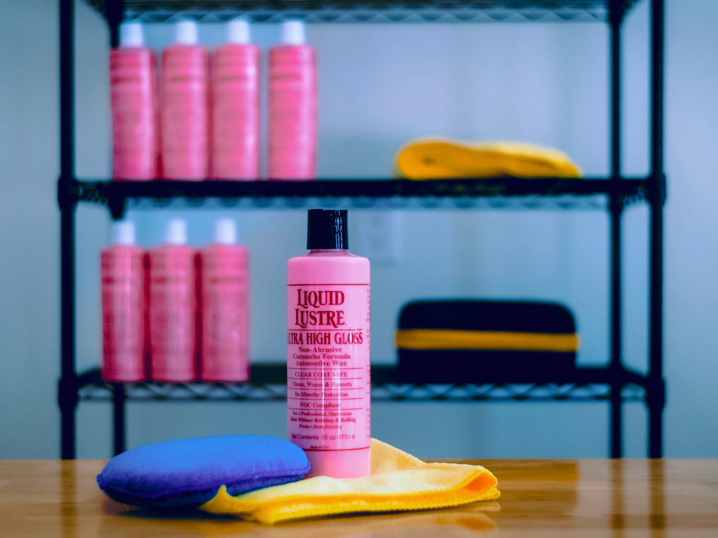 A bottle of The Liquid Lustre Original Pink Wax on a table with shelves in the background